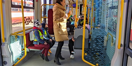 Powiększ grafikę: Dzieci siedzą w tramwaju, pani stoi na środku i opowiada.