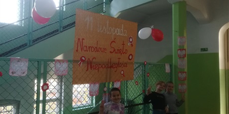 Powiększ grafikę: Zdjęcie przedstawiające pracę i plakat wykonane przez dzieci i wychowawców z okazji Narodowego Święta Niepodległości. Trzy uczennice pokazujące znak pokoju.